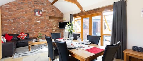 A dining area with a brick wall, wooden beams, a table set for two, and a view through a window.