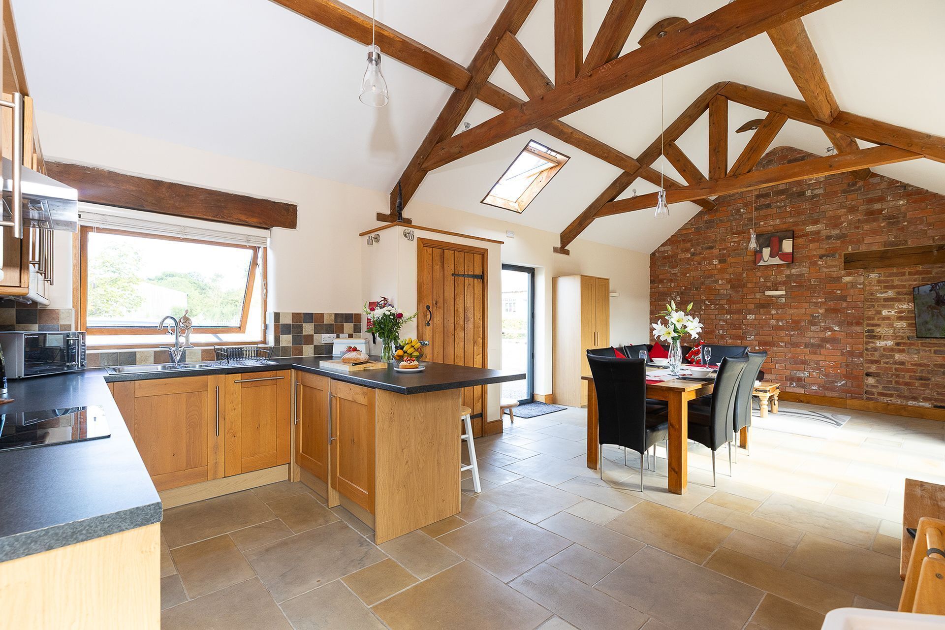 A spacious kitchen with wooden cabinets, a large island, and a dining area with a brick wall and modern furniture.