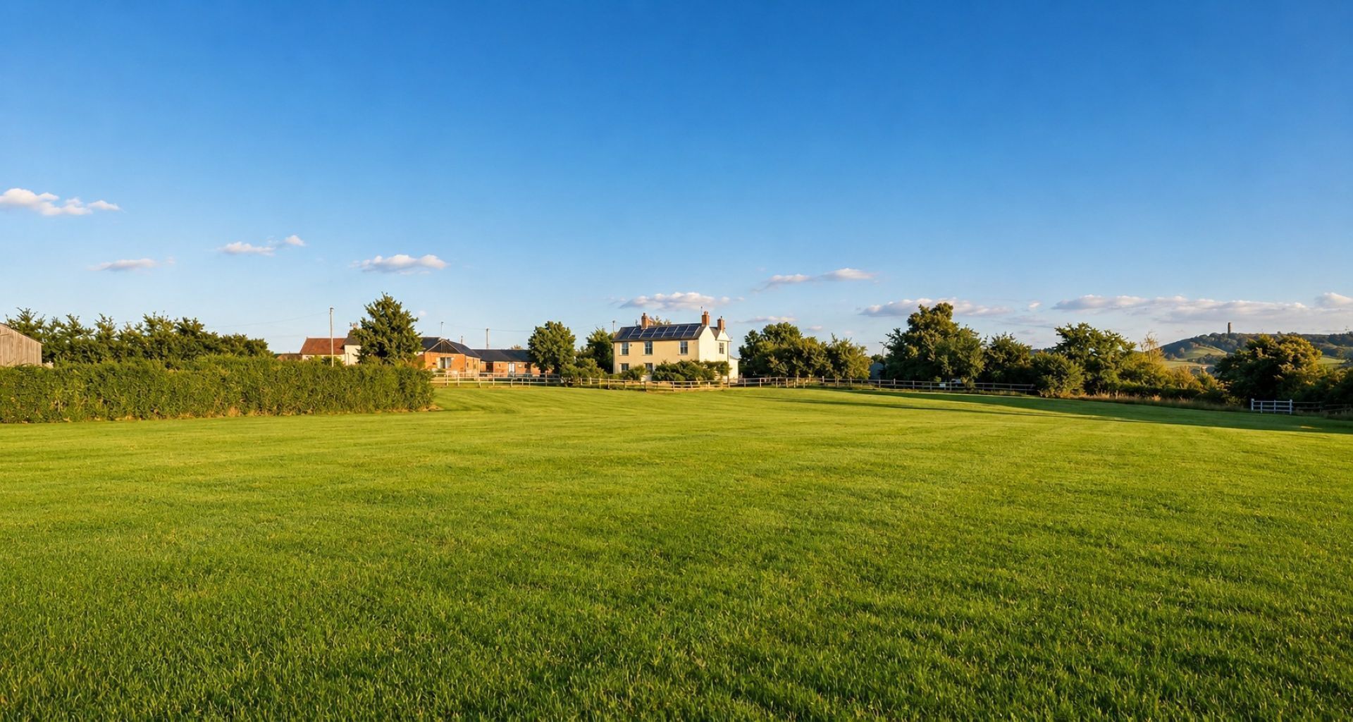 A large green field with a house in the background.
