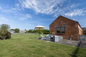 Ein Backsteinhaus mit Terrassengelände, Sitzgelegenheiten im Freien und einem großen Sonnenschirm.