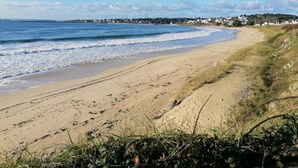 Una playa con arena, olas y un pueblo a lo lejos.