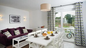 Una sala de estar moderna con sofá, mesa de centro, mesa de comedor y sillas. Hay una ventana con cortinas, una bicicleta afuera y un cuadro en la pared.