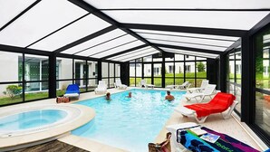 Una piscina interior cubierta con paredes de vidrio, sillas de descanso y un jacuzzi.