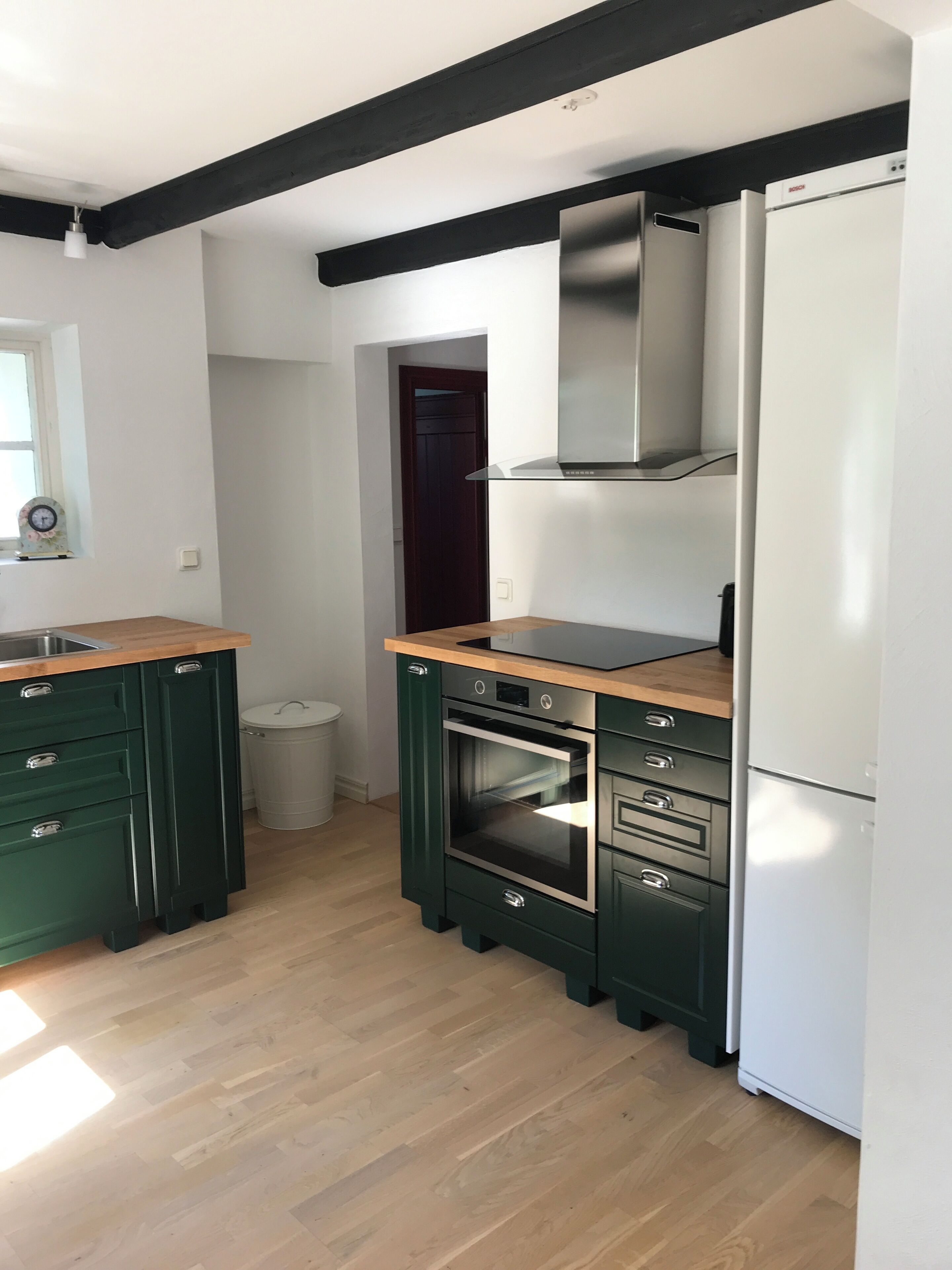 Una cocina con armarios verde oscuro, un horno de acero inoxidable, un refrigerador blanco y una encimera de madera.