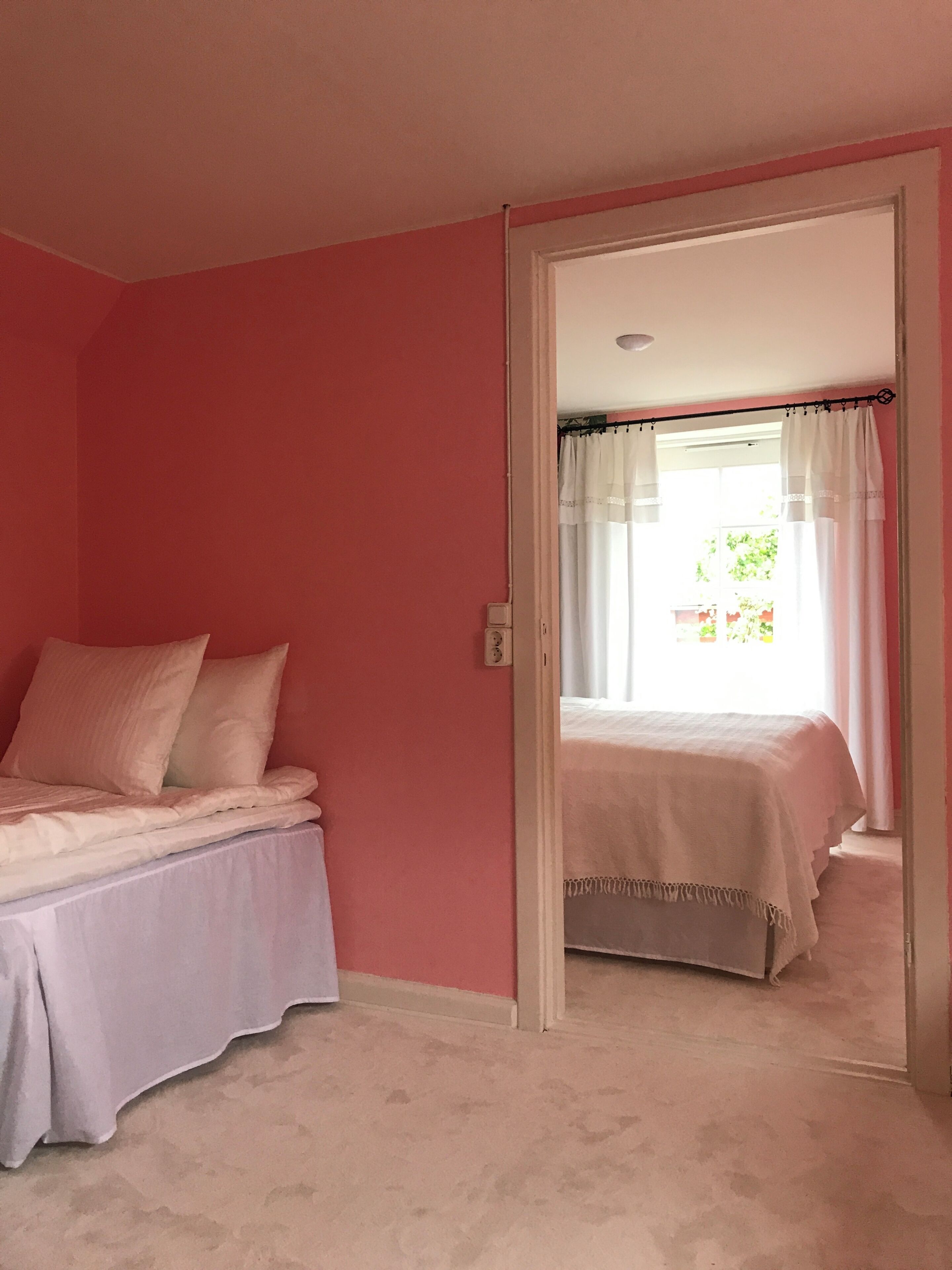A bedroom with a bed, a door leading to another room, and a window with curtains.