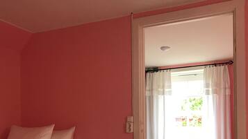 A bedroom with a bed, a door leading to another room, and a window with curtains.