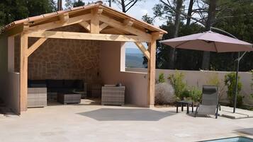 A covered outdoor area with a stone wall, a pool, and a patio with a table and chairs.