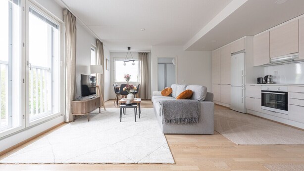 A modern living room with a sofa, TV, dining table, and kitchen area. - Modern Downtown 2BR Apartment & Sauna (Kuopio)