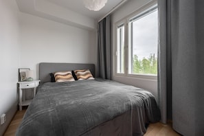 Une chambre à coucher moderne avec un grand lit, une table de chevet, une commode et une fenêtre avec des rideaux.