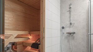 A sauna room with a wooden bench, a bench with a towel, and a shower area with a glass door. - Modern Downtown 2BR Apartment & Sauna (Kuopio)