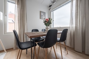 Un coin repas avec une table en bois, des chaises noires, un vase rempli de fleurs et un tableau accroché au mur.