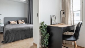 A modern bedroom with a bed, bedside table, and a desk with a chair. - Modern Downtown 2BR Apartment & Sauna (Kuopio)