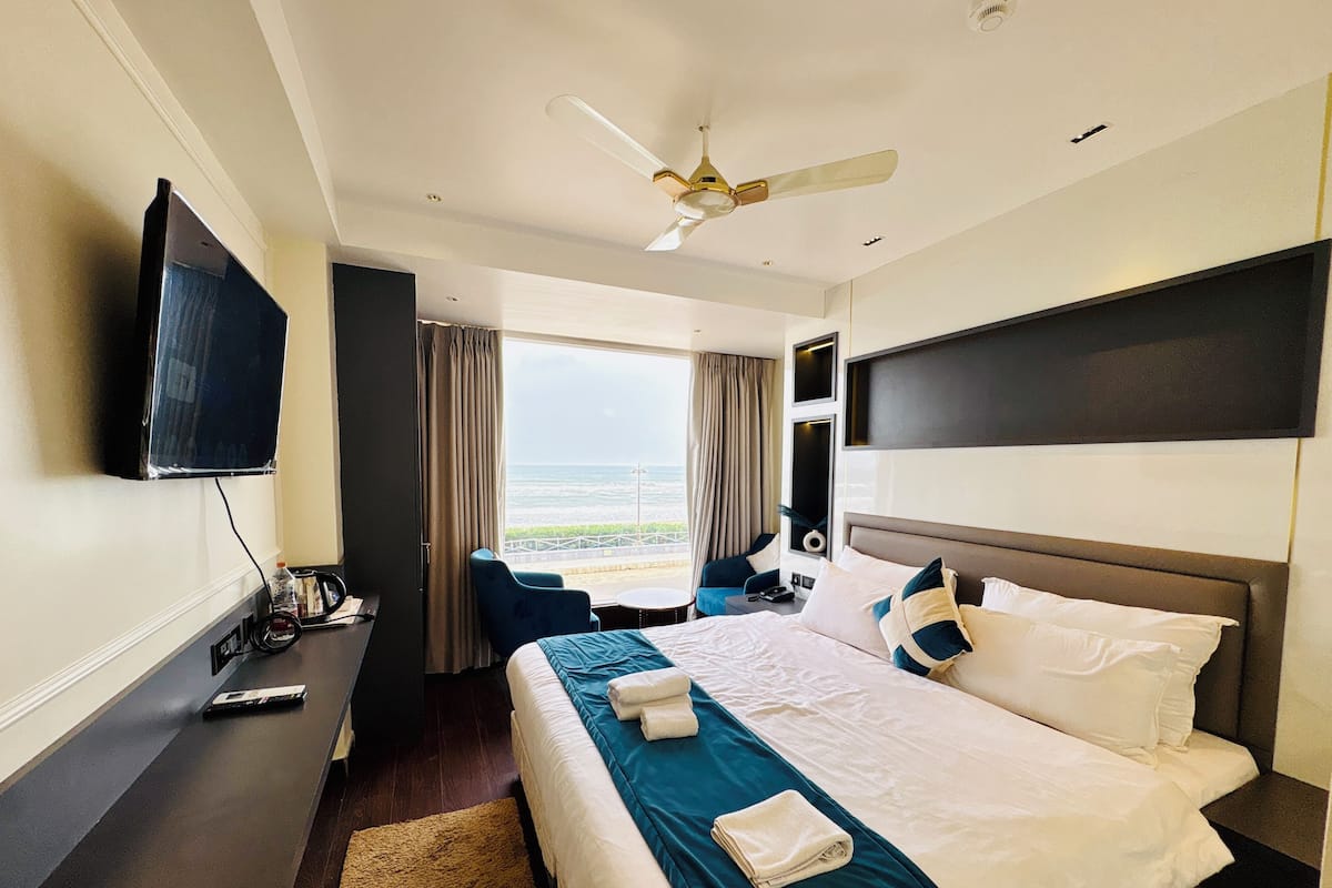 A hotel room with a bed, a desk, a chair, a TV, and a view of the ocean.