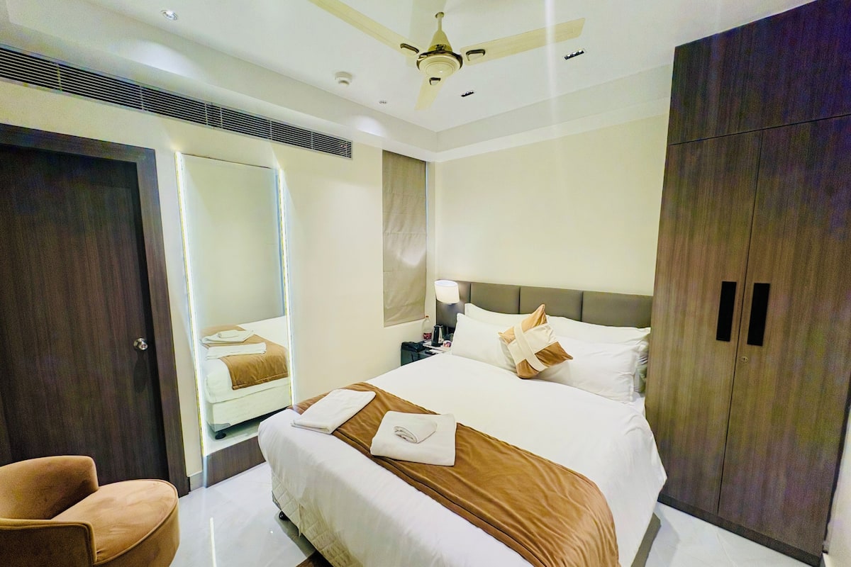 A modern hotel room with a large bed, a ceiling fan, a wardrobe, and a seating area.