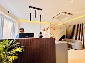 A reception desk with a laptop, a potted plant, and a flag. - Eastern Dhaam New Marine Drive Rd (Brahmagiri)