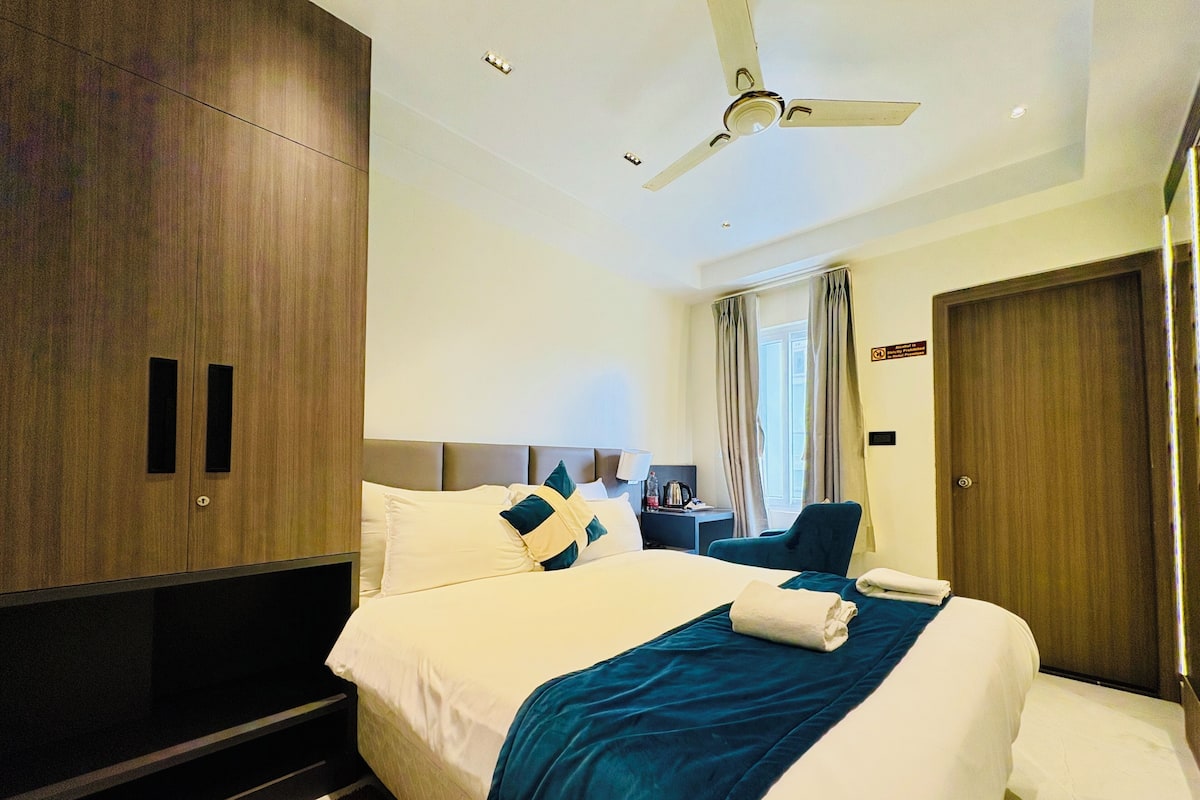 A hotel room with a bed, a desk, a chair, a wardrobe, and a ceiling fan.