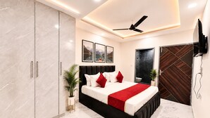 A modern bedroom with a bed, wardrobe, ceiling fan, and artwork. - Mauryan Signature Hotel NHPC Metro (Faridabad)