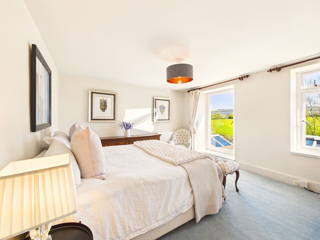 A bedroom with a bed, a bedside table, a lamp, a chair, and a window with a view of the outdoors.