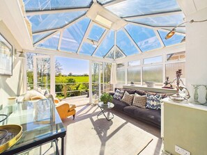 Une véranda avec un toit en verre, un canapé, une table basse et une vue sur l’extérieur.