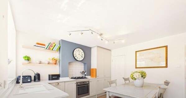 A modern kitchen with a clock, a dining table, and a white cabinet. - Winchcombe Cottage with breathtaking views (Winchcombe)