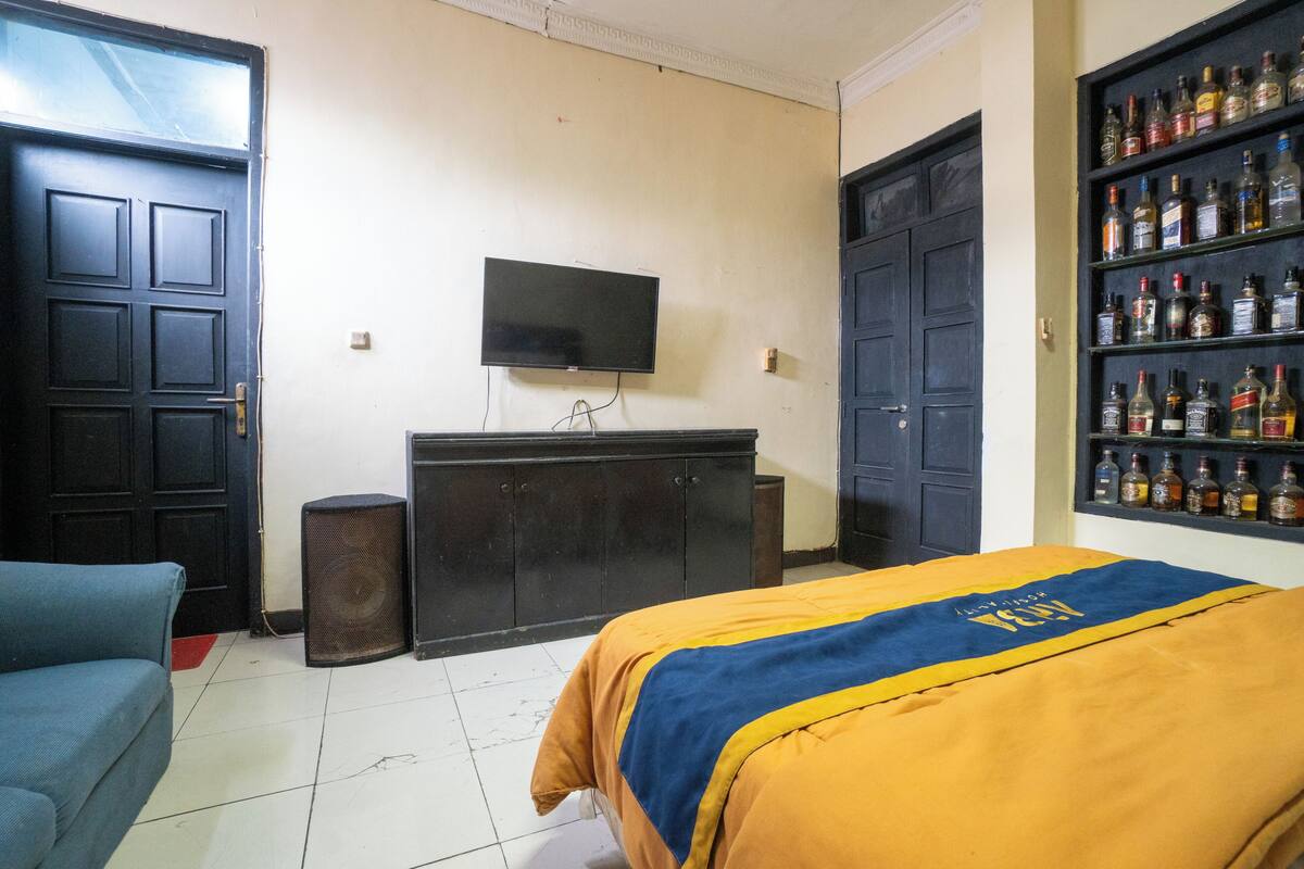 Ein Zimmer mit einem Bett, einem Fernseher, einem Schrank und einem Regal mit Flaschen.