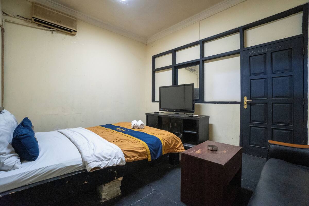 Ein Zimmer mit einem Bett, einem Fernseher auf einem Schrank, einem kleinen Tisch und einer Tür.