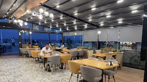 An outdoor café with tables and chairs, a tiled floor, and a view of the sea.