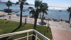A coastal promenade with palm trees, a clear sky, and boats on the water.
