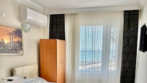 A hotel room with two beds, a wardrobe, a desk, a chair, a heater, a window with curtains, and a wall-mounted air conditioner.
