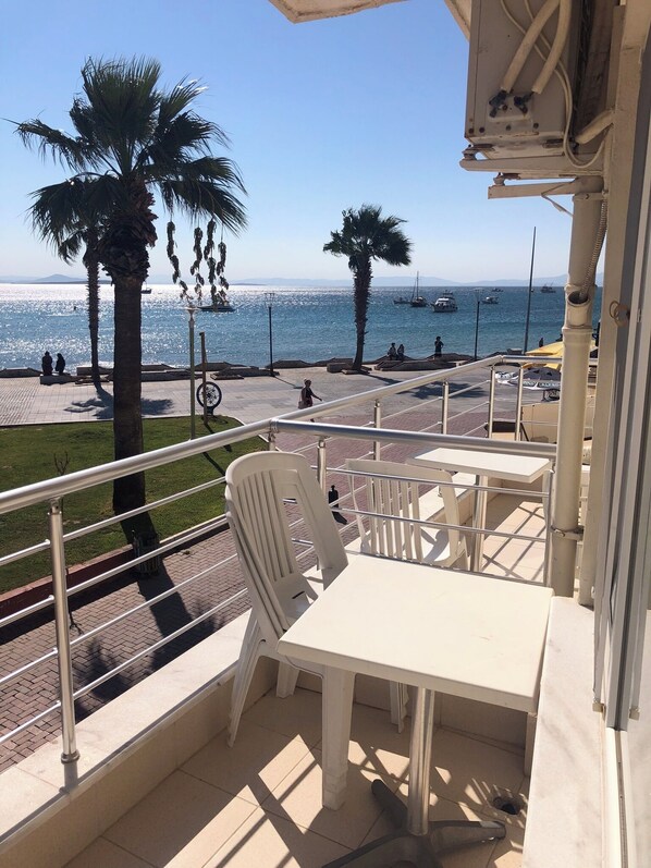 Un balcon avec une table et des chaises, donnant sur une plage bordée de palmiers et de bateaux.