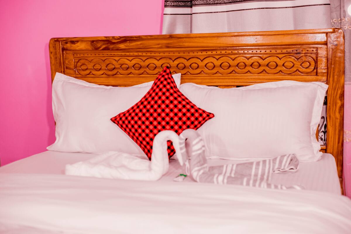 A bed with a wooden headboard, white bedding, a red and black checkered pillow, and a white swan decoration.
