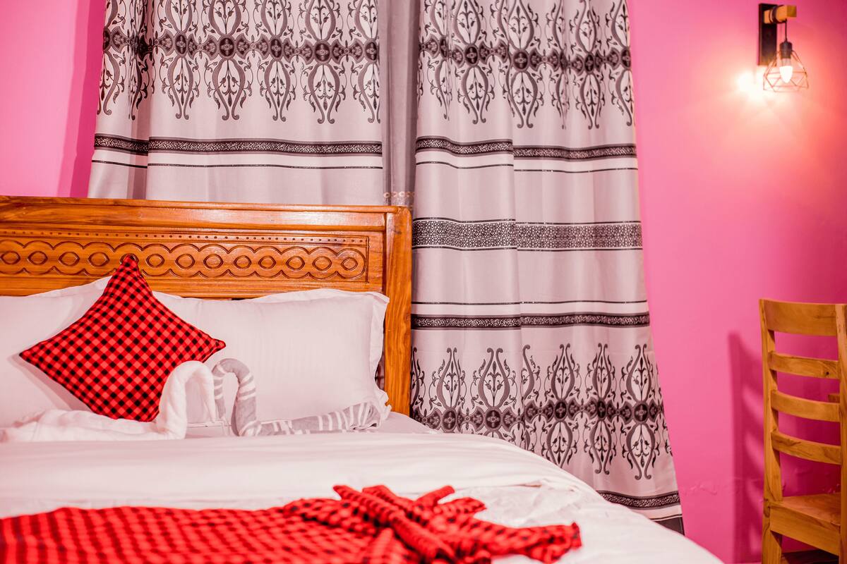 A bed with a checkered pillow, a wooden headboard, and a red blanket.