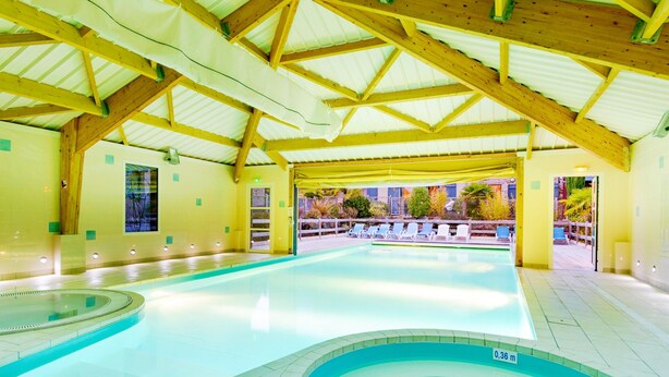 A swimming pool with a tiled floor, a diving area, and a covered seating area with chairs. - Charming Breton Duplex Cottage (Cancale)