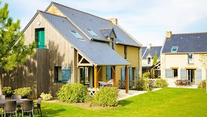 A two-story house with a sloped roof, a wooden exterior, and a fenced backyard with outdoor furniture. - Charming Breton Duplex Cottage (Cancale)