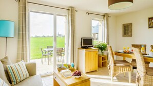 A living room with a sofa, coffee table, TV, and dining area with wicker chairs and a table set for breakfast. - Charming Breton Duplex Cottage (Cancale)