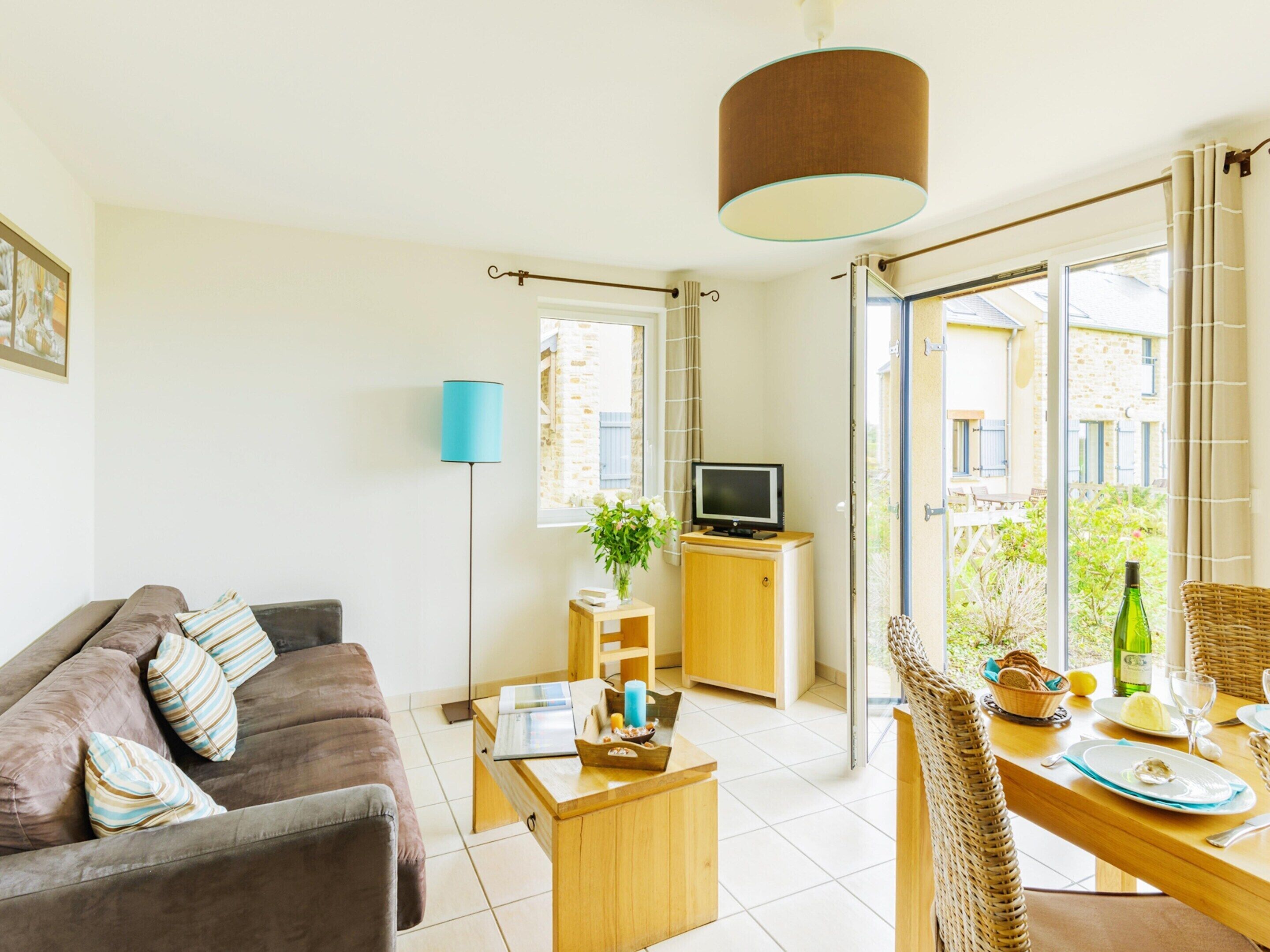 Ein Wohnzimmer mit Sofa, Couchtisch, Fernseher und einem Essbereich mit Tisch für zwei Personen.