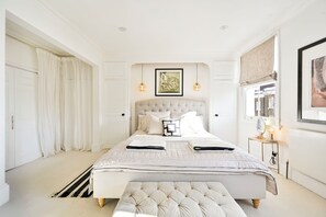 A spacious bedroom with a large bed, a bedside table with a lamp, and a window with a view. - Chelsea Town House, Designer Kitchen + Primary Suite. Minutes to the Kings Road. (London)