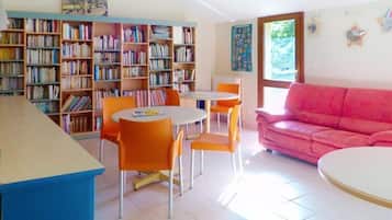 Ein Zimmer mit Bücherregal, einem rosafarbenen Sofa und einem Essbereich mit orangefarbenen Stühlen.