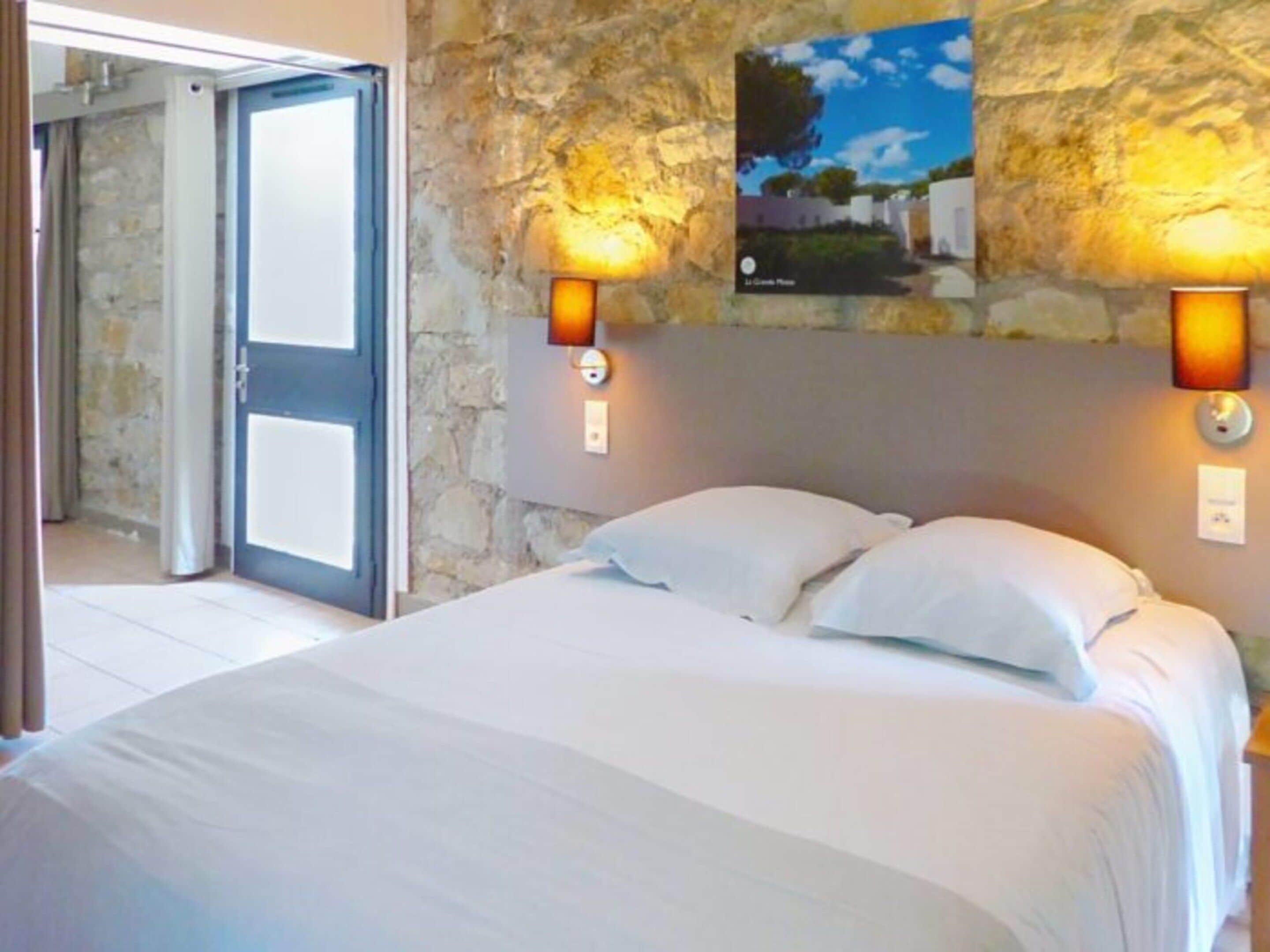 Ein Schlafzimmer mit Steinwand, einem Bett mit weißer Bettwäsche und zwei Wandleuchten.