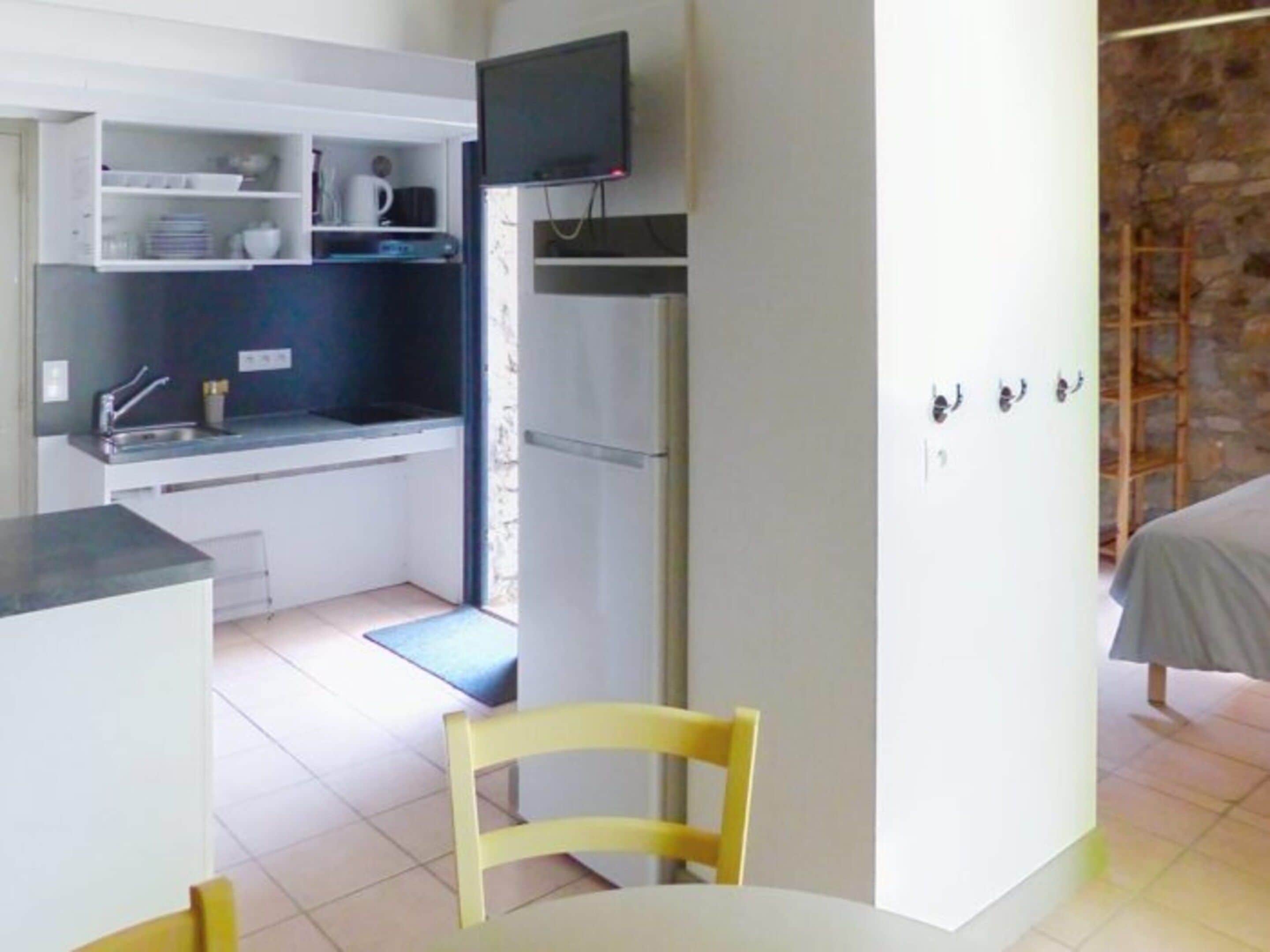 A compact kitchen with a refrigerator, a sink, and a flat-screen TV mounted above it.