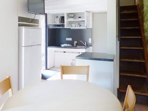 Cozinha compacta com área de refeições, TV integrada e escada.