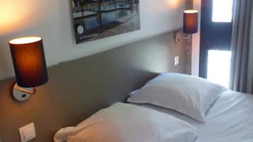 Une chambre d’hôtel avec un lit, deux lampes fixées au mur, un tableau représentant un port de plaisance et une fenêtre avec des rideaux.