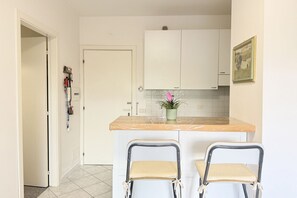 A kitchen with white cabinets, a marble countertop, two chairs, and a potted plant.