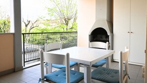 A balcony with a white table and blue cushioned chairs, a black grill, and a white door.