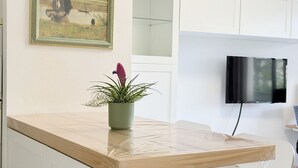 A kitchen with a wooden countertop, a potted plant, a framed painting, and a TV mounted on the wall.