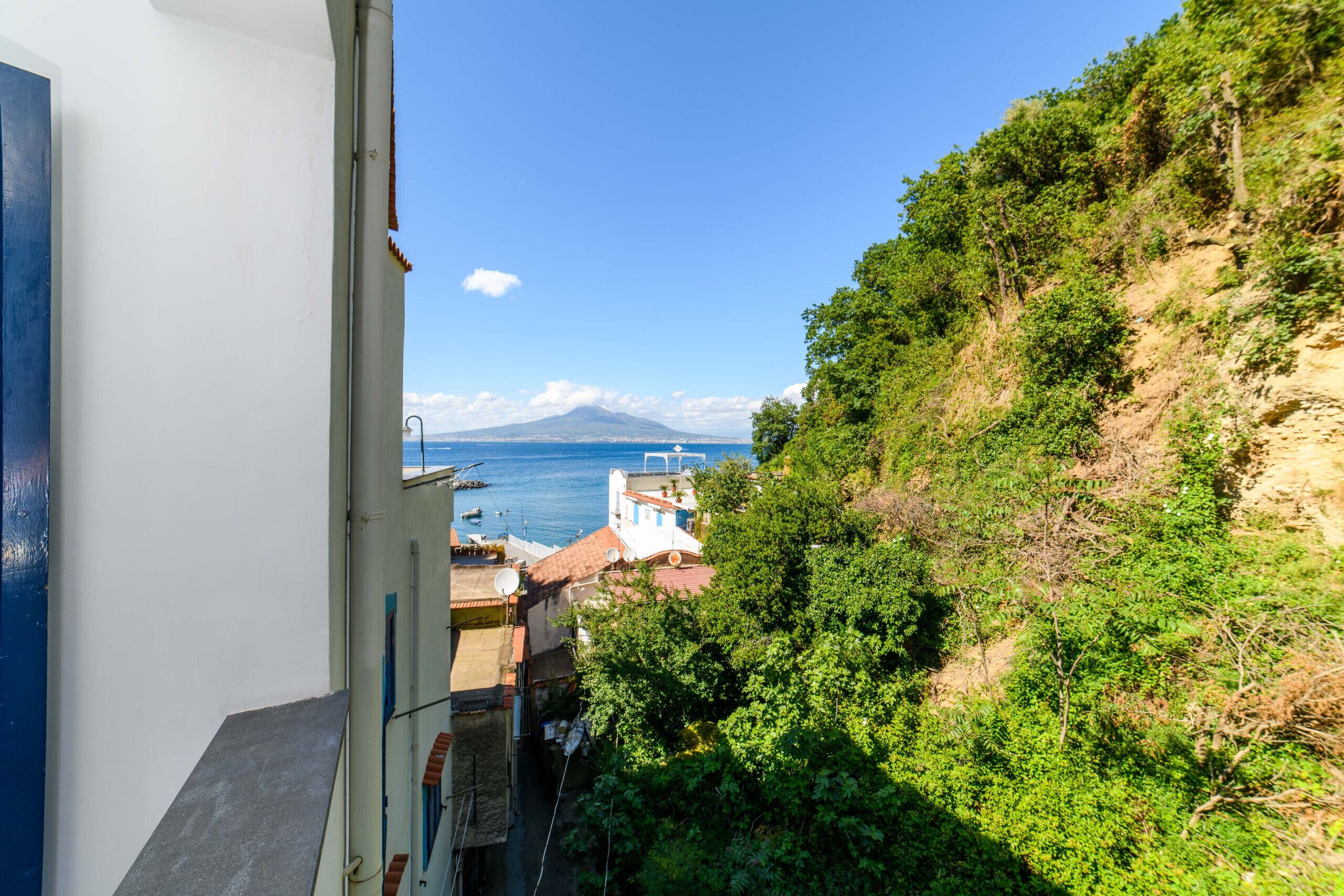 Un balcon donnant sur une zone côtière, avec des bâtiments, de la végétation et une montagne visible au loin.