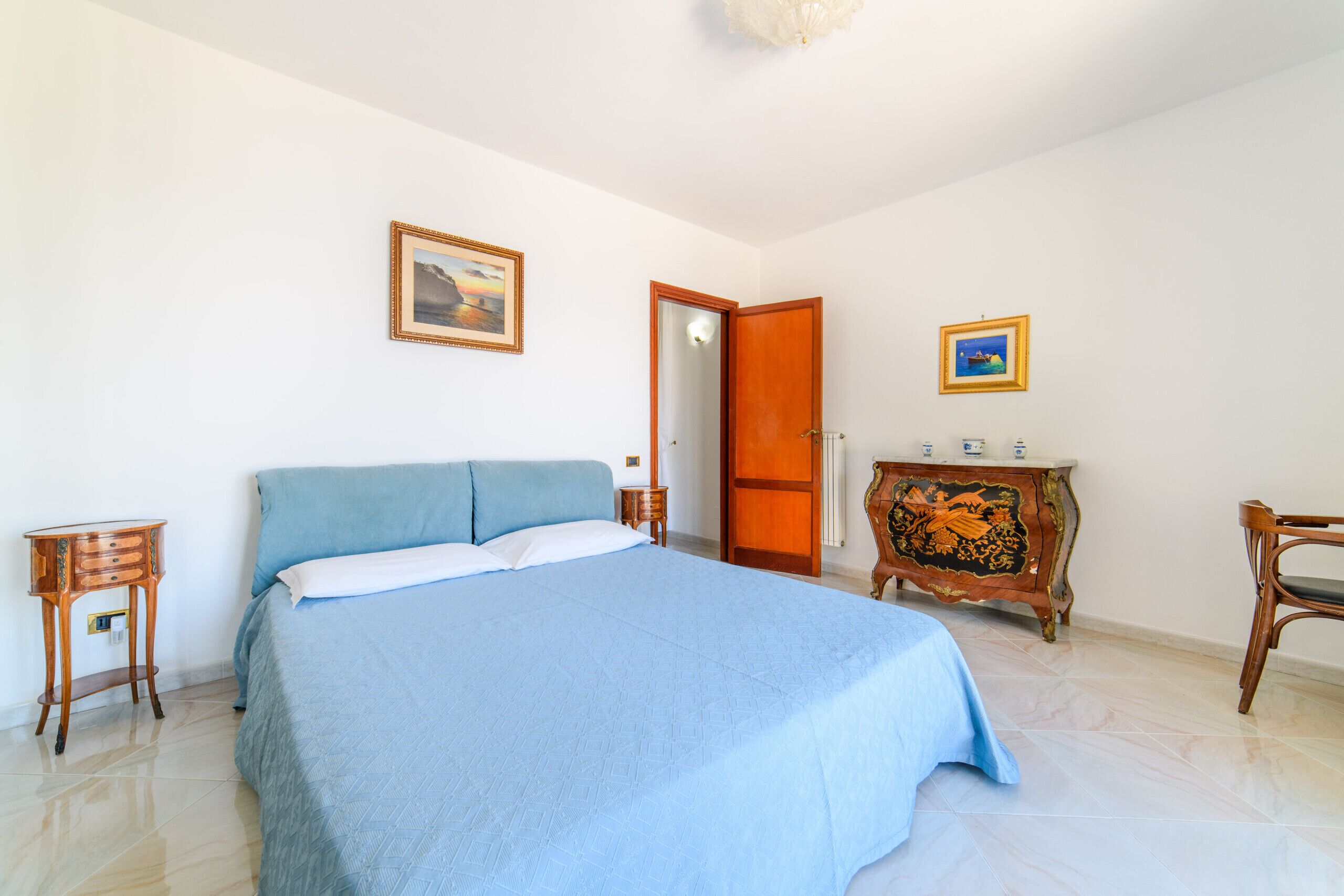Une chambre à coucher avec un lit, une commode, une chaise et deux tableaux accrochés au mur.