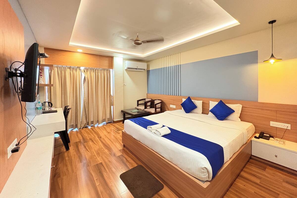 Habitación de hotel con cama, mesita de noche, escritorio, televisor y ventilador de techo.