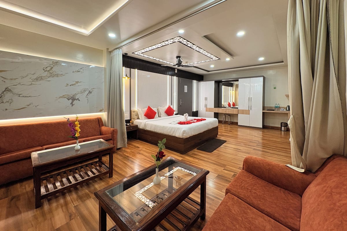Una habitación de hotel moderna con un sofá, una mesa de centro de vidrio, una cama con almohadas rojas, un escritorio y un espejo.