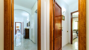 Um corredor com porta de madeira, paredes brancas e chão de azulejos.
